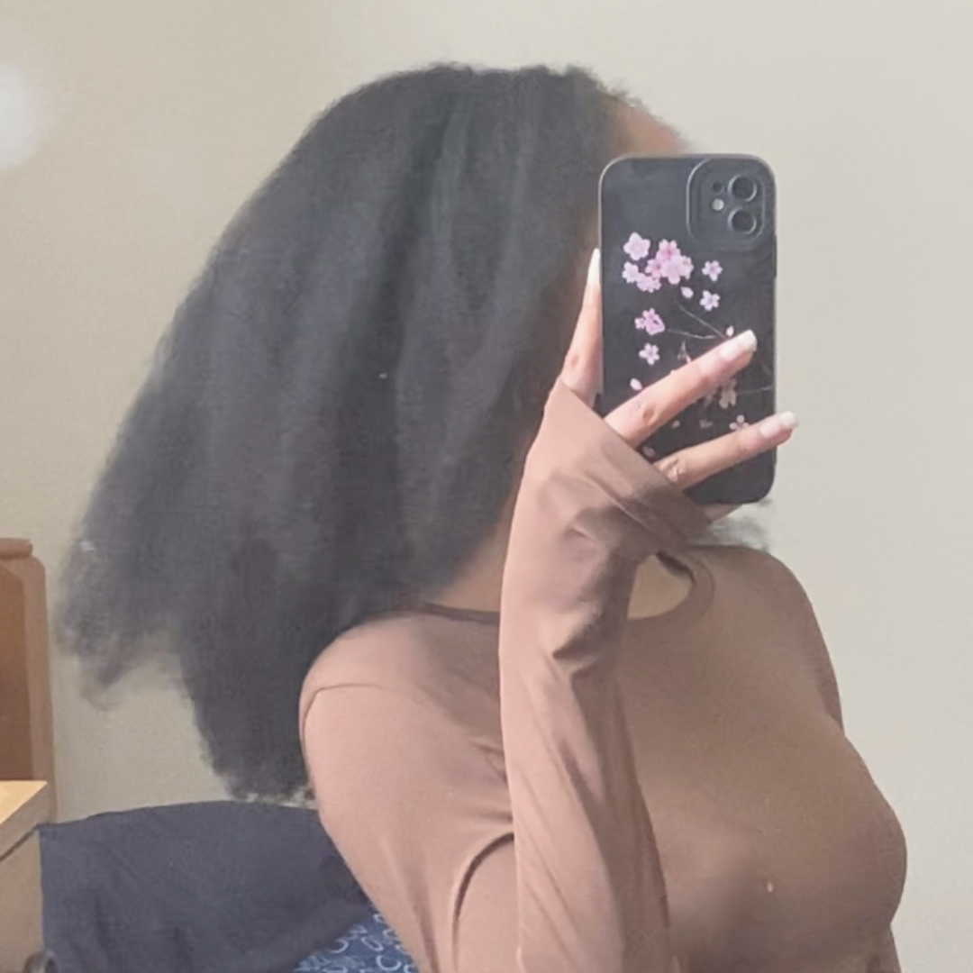 A picture of my long, 4c, type 4 natural hair in a blow out style. I am facing the side and I am wearing a brown top with my face covered by my phone. My natural type 4 hair is black with and goes past my shoulders in the blow out state. It is relatively full.